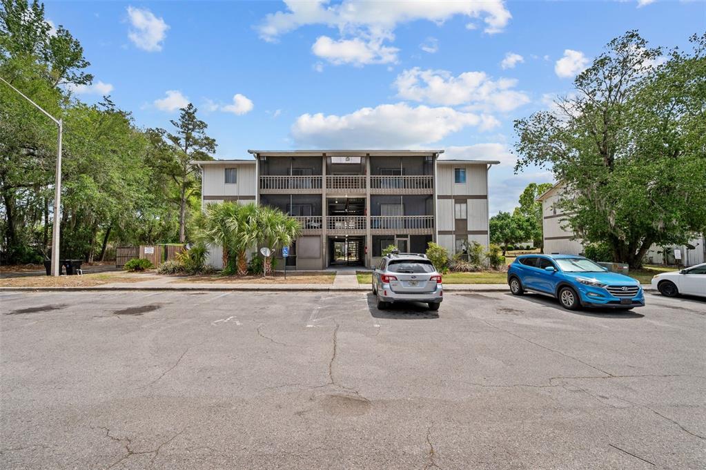 A three-story apartment building with screened balconies sits behind a paved parking lot — 6519 W NEWBERRY ROAD UNIT 1111, GAINESVILLE, FL