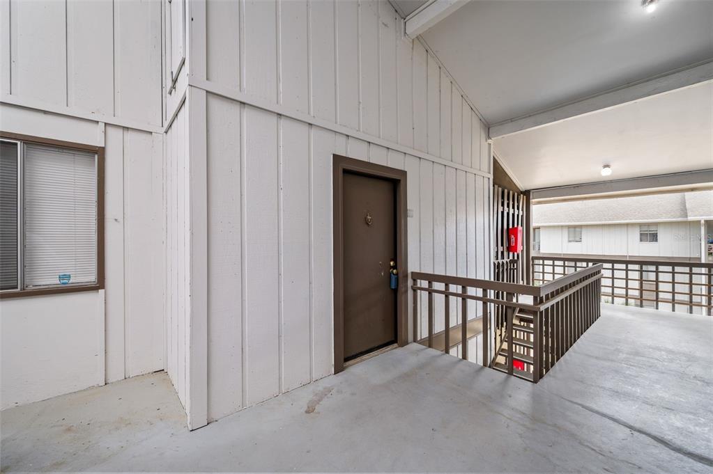 An exterior view of a building entrance with a brown door and a wooden railing — 6519 W NEWBERRY ROAD UNIT 1111, GAINESVILLE, FL