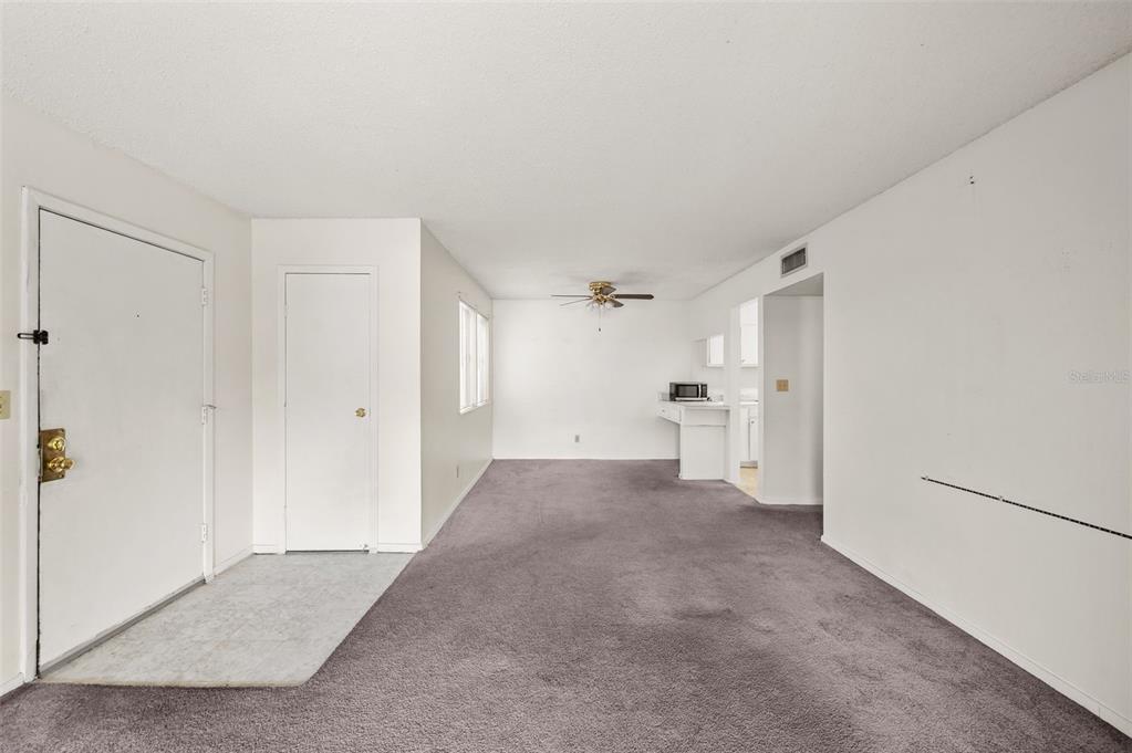 An empty living room with gray carpet, white walls, a ceiling fan, and a doorway — 6519 W NEWBERRY ROAD UNIT 1111, GAINESVILLE, FL