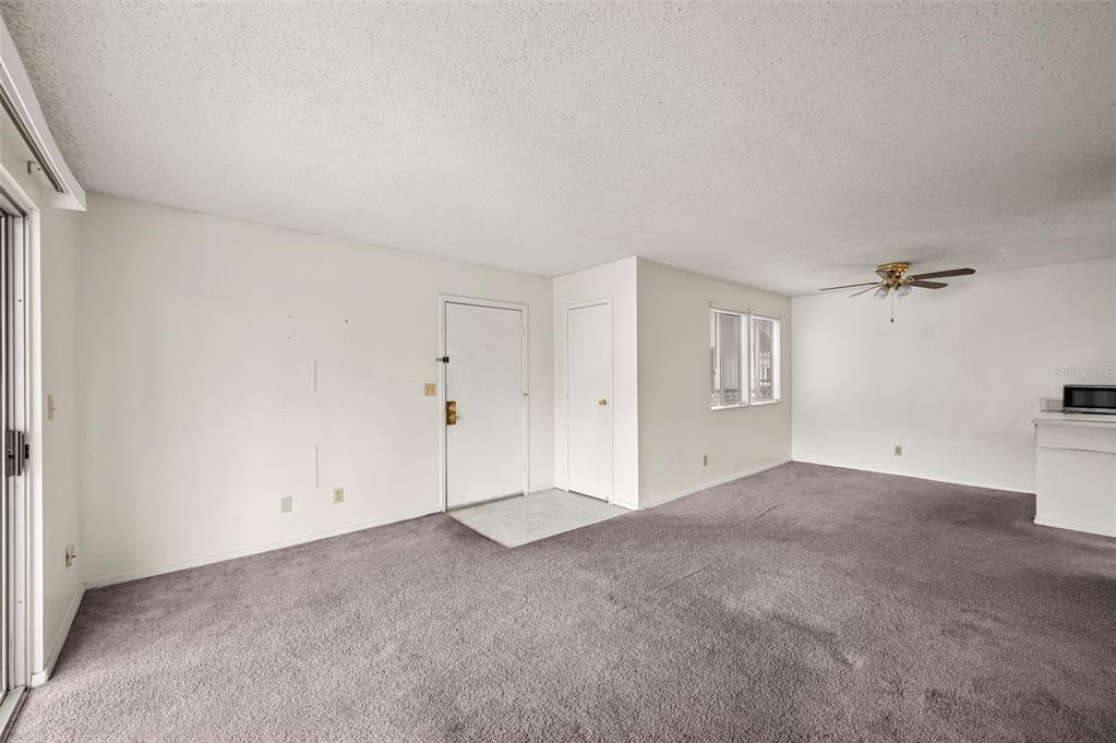 An empty living room features gray carpeting, white walls, a ceiling fan, and a door — 6519 W NEWBERRY ROAD UNIT 1111, GAINESVILLE, FL