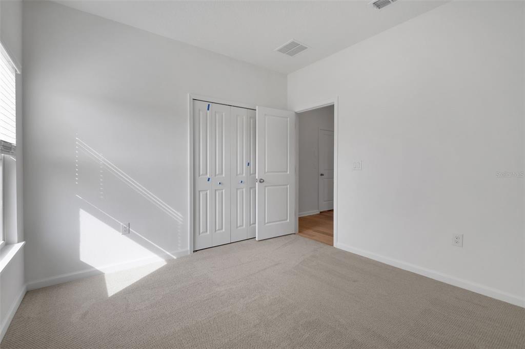A bedroom with beige carpet, white walls, a white closet, and an open doorway — 167 LAKE FRANCES DRIVE, ST AUGUSTINE, FL