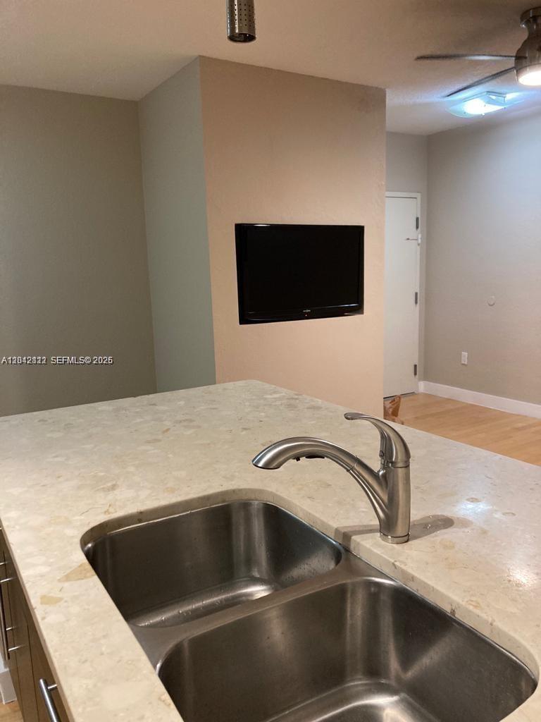 A kitchen island with a double-basin stainless steel sink sits before a wall-mounted television — 7171 Bay Dr # 9, Miami Beach FL 33141, MIAMI BEACH, FL