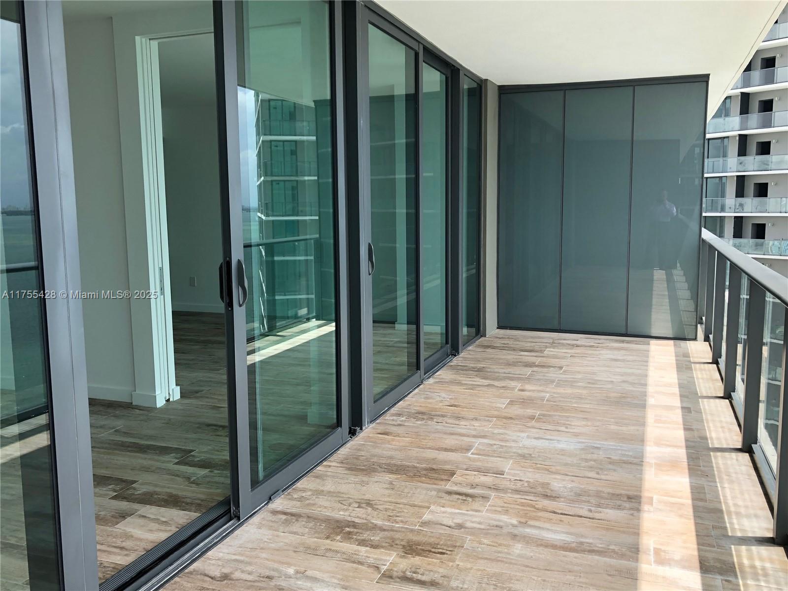 A balcony with wood-look tile flooring features large glass sliding doors and a glass railing — 650 NE 32nd St # 2006, Miami FL 33137, MIAMI, FL