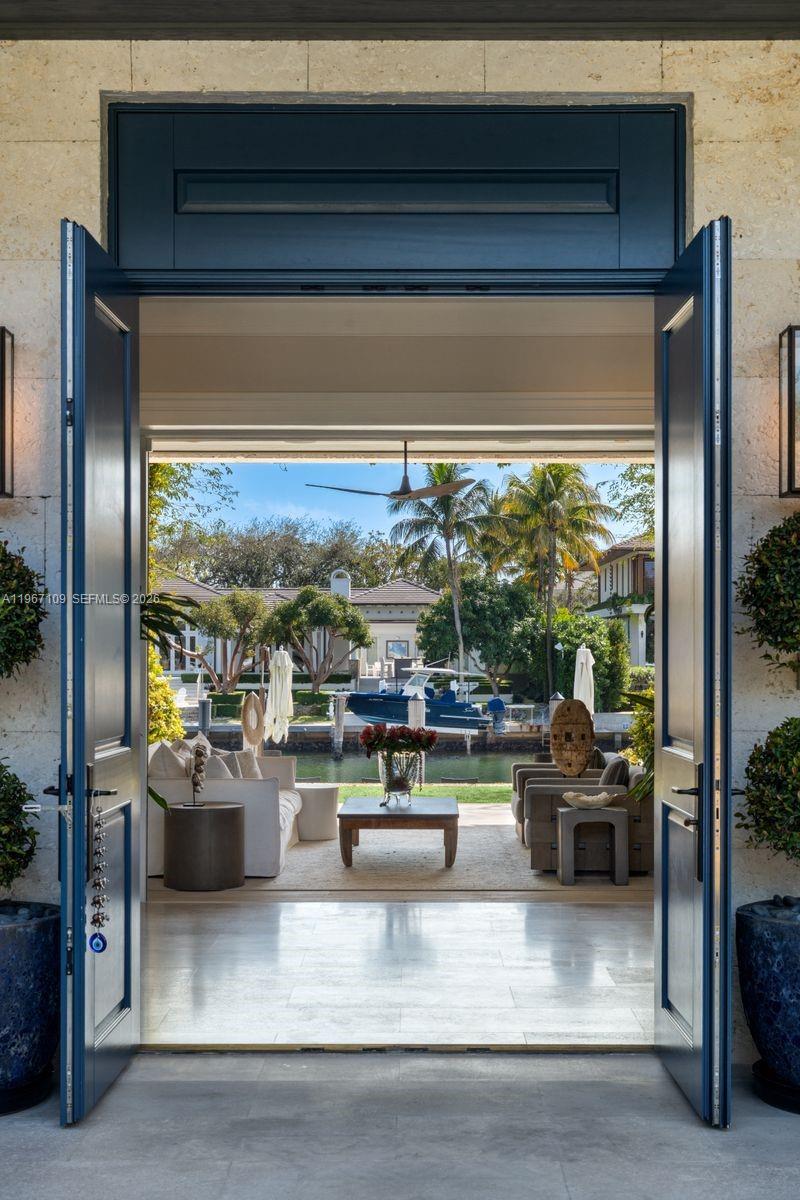 A view through open blue doors into a patio area overlooking a canal and boat — 550 Marquesa Dr, Coral Gables FL 33156, CORAL GABLES, FL