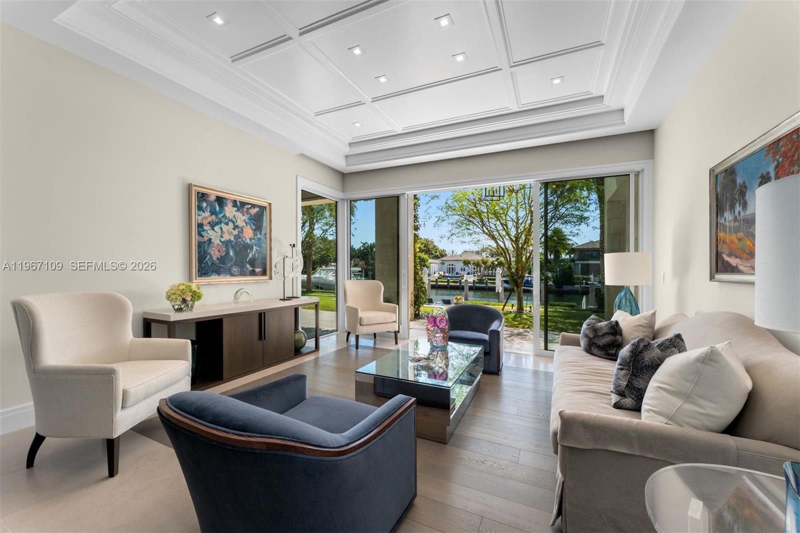 A living room features a coffered ceiling, glass sliding doors, and a view of water — 550 Marquesa Dr, Coral Gables FL 33156, CORAL GABLES, FL
