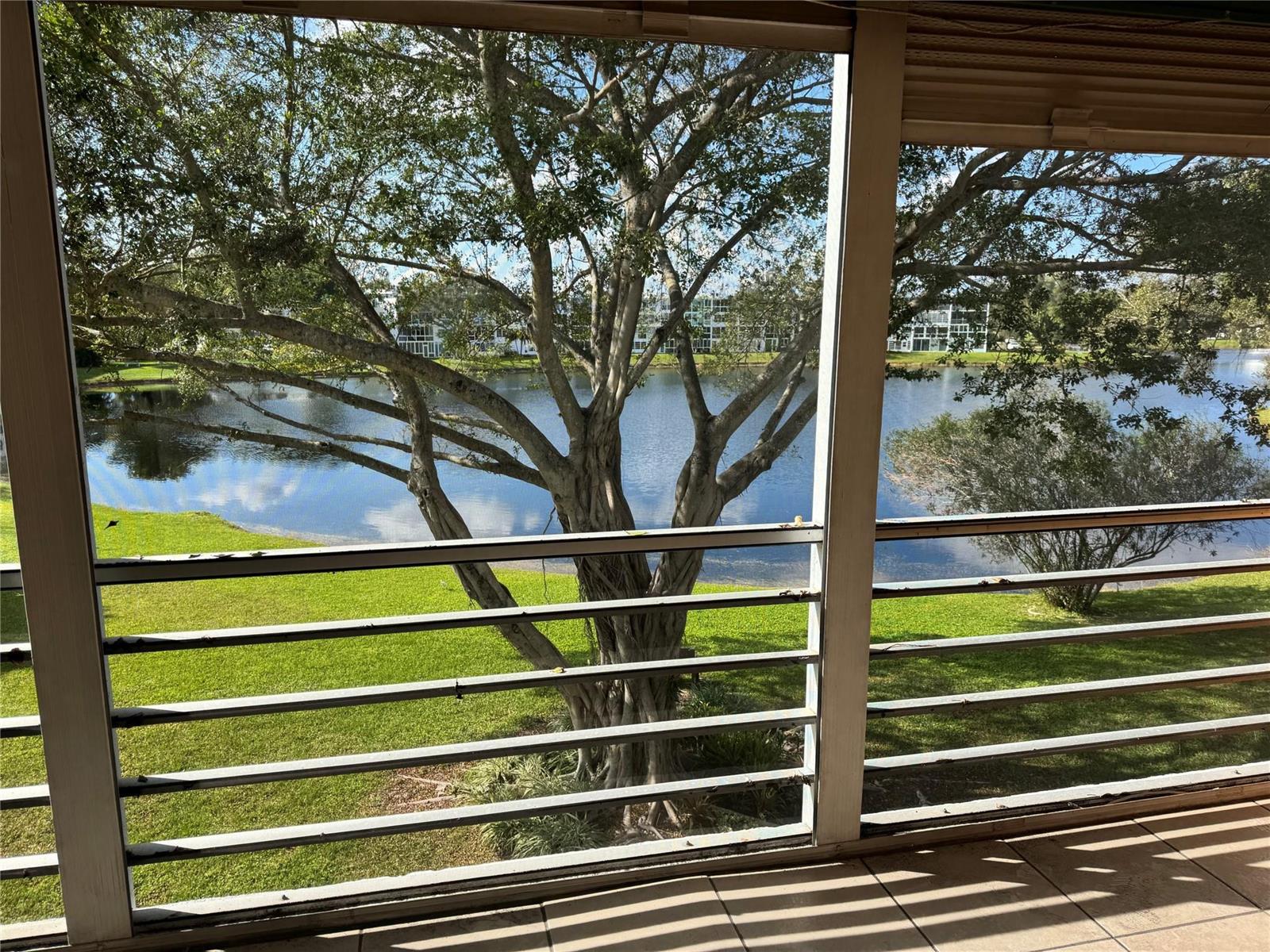 A screened-in balcony overlooks a grassy lawn, a lake, and trees — 3058 Cambridge C # 3058, Deerfield Beach FL 33442, DEERFIELD BEACH, FL