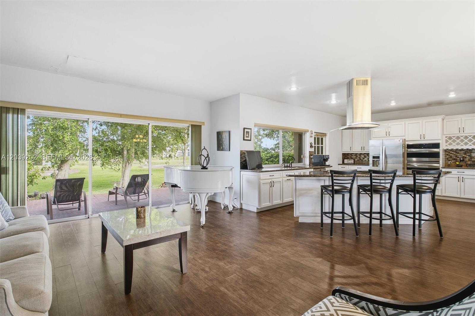 An open-concept kitchen and living area features a white grand piano and sliding glass doors — 19015 E Saint Andrews Dr, Hialeah FL 33015, HIALEAH, FL