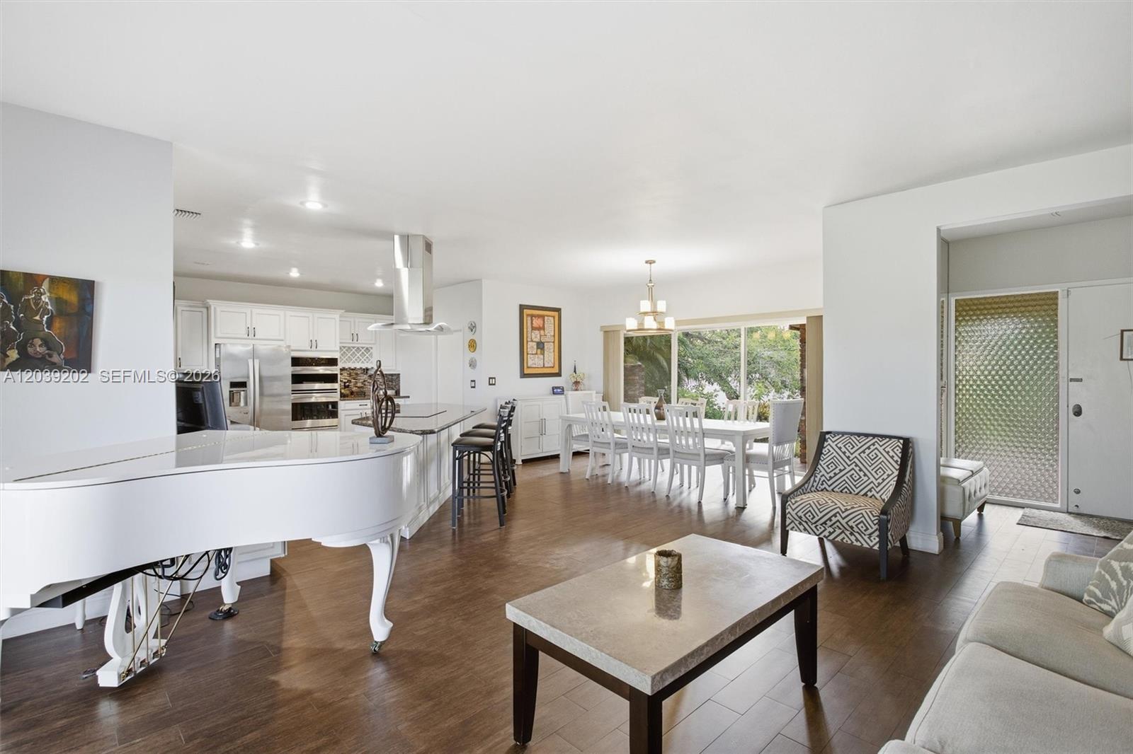 An open-concept living and dining area features a white grand piano and dark wood flooring — 19015 E Saint Andrews Dr, Hialeah FL 33015, HIALEAH, FL