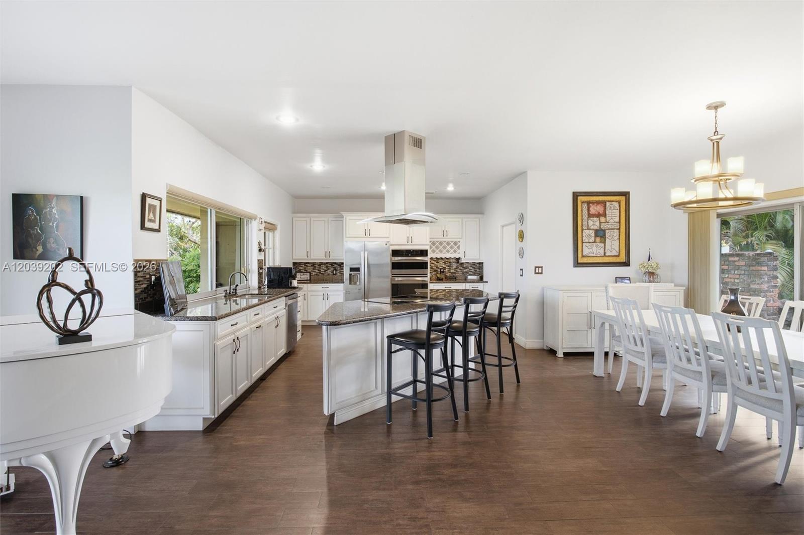 A white kitchen with a center island and dining area features dark wood flooring — 19015 E Saint Andrews Dr, Hialeah FL 33015, HIALEAH, FL