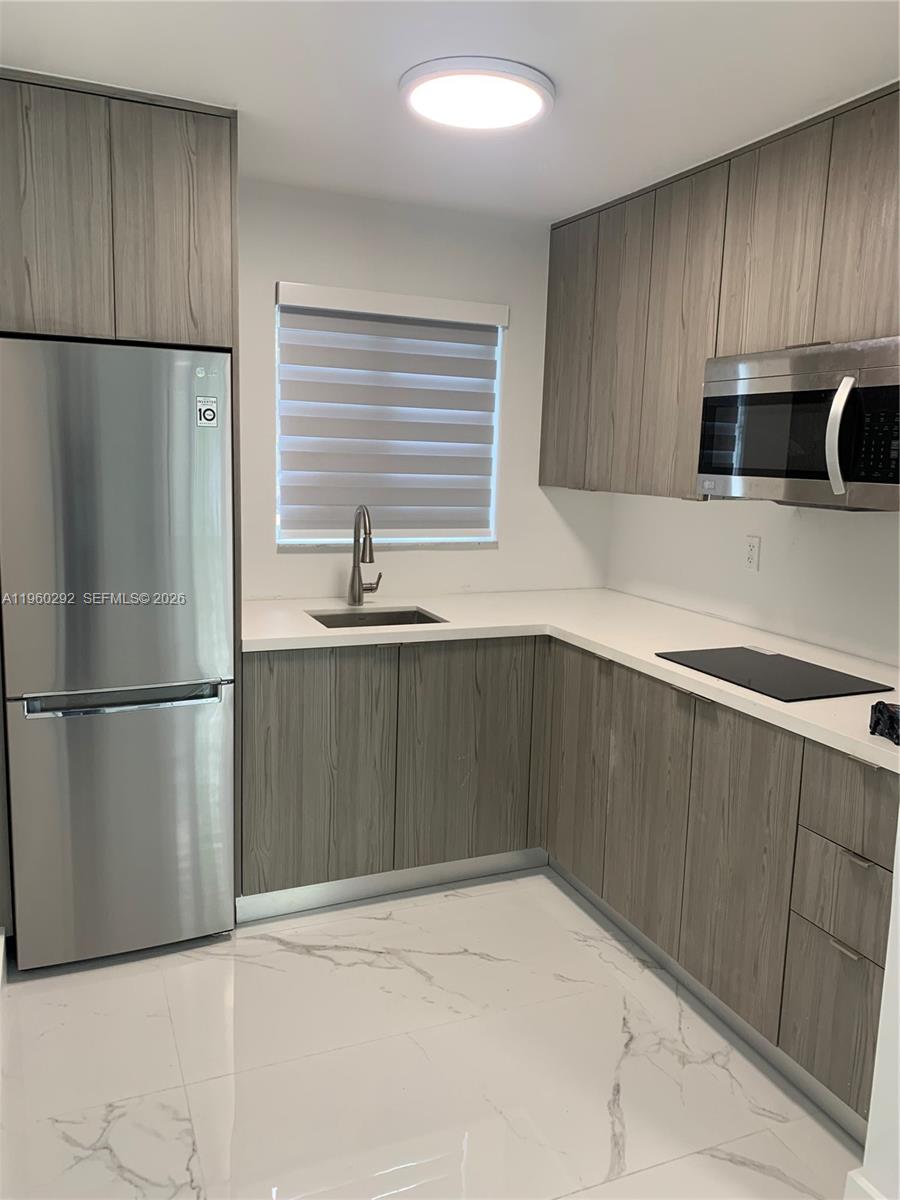 A modern kitchen features wood-grain cabinets, stainless steel appliances, and white marble-style flooring — 7843 NE 10th Ave # 2, Miami FL 33138, MIAMI, FL