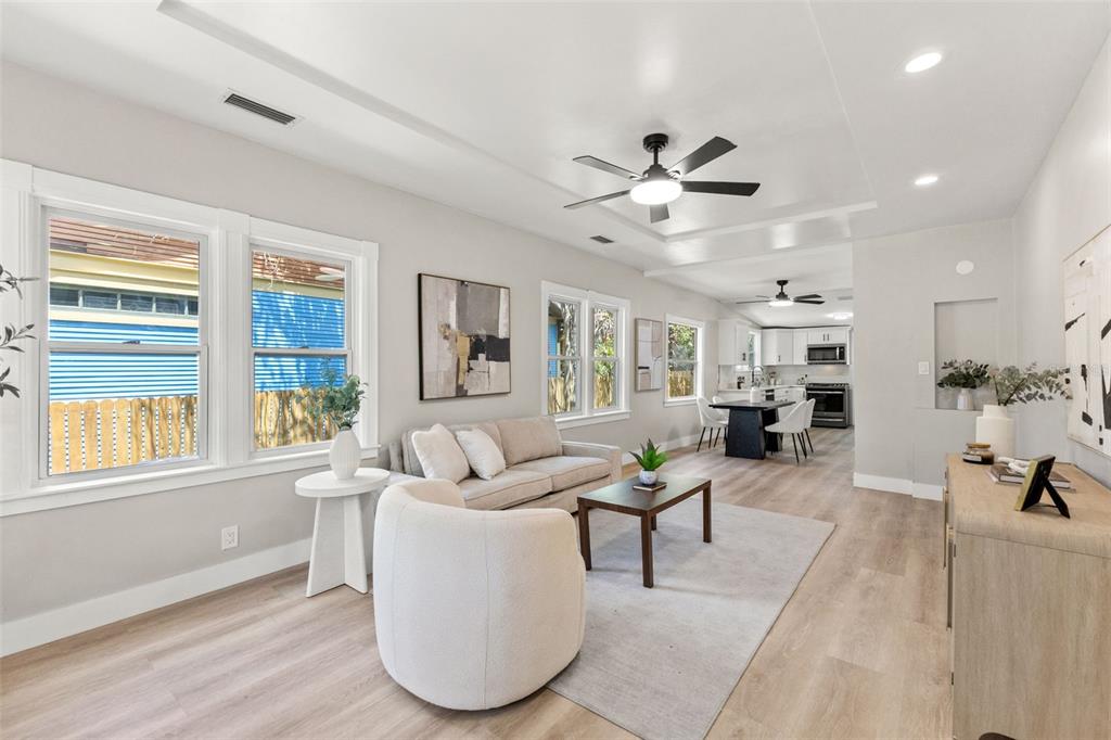 A bright living room features light wood flooring, a neutral sofa, and an open kitchen — 604 E LAMBRIGHT STREET, TAMPA, FL