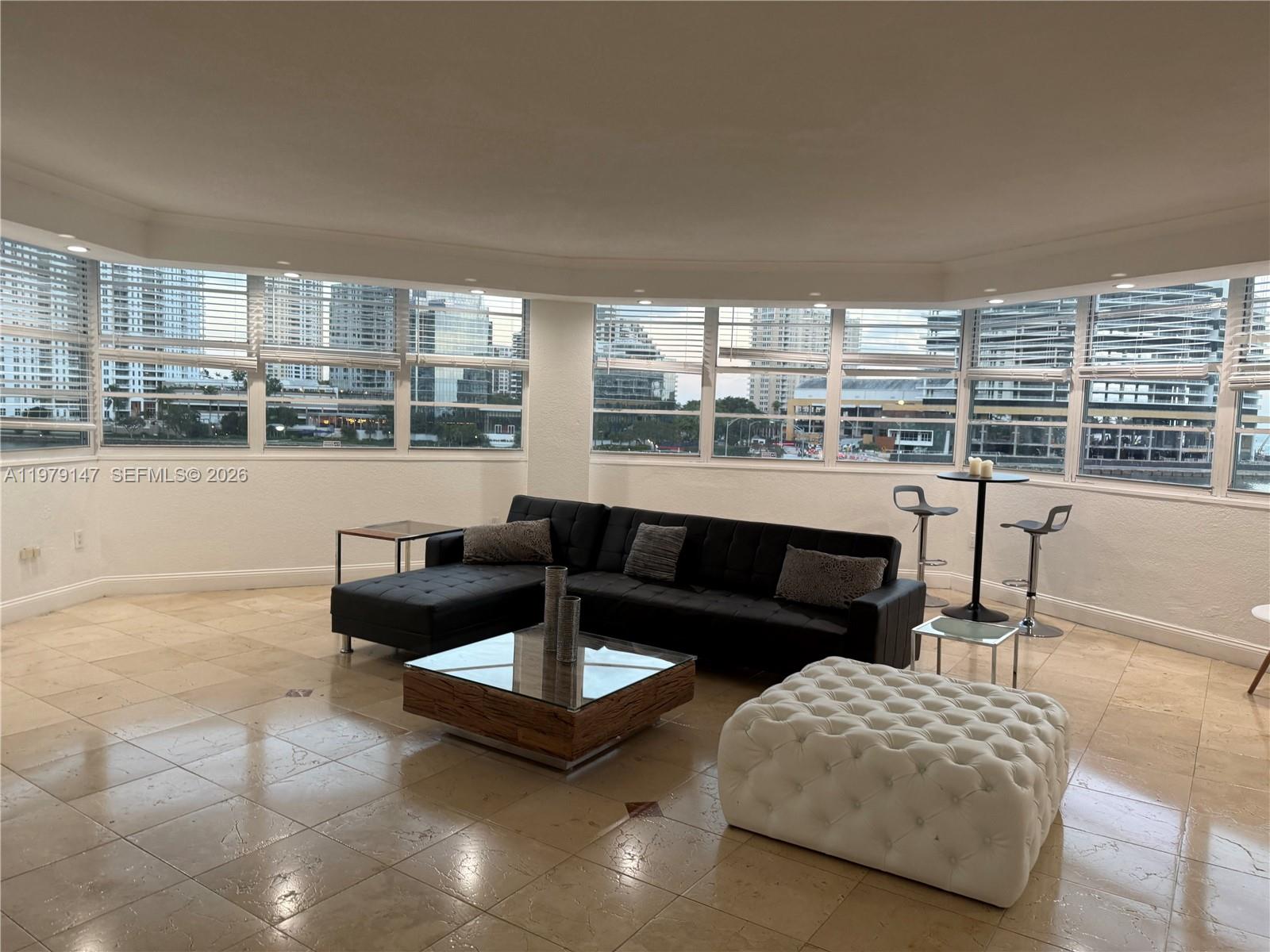 A living room features a black sectional sofa, glass coffee table, and panoramic city views — 801 Brickell Bay Dr # 470, Miami FL 33131, MIAMI, FL