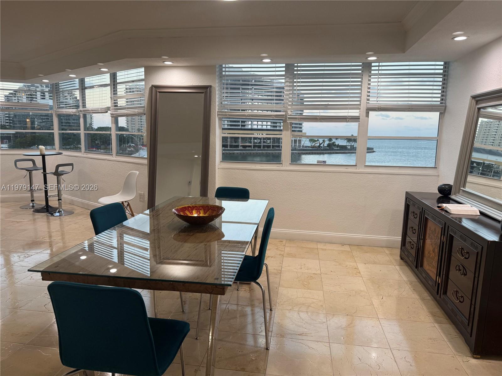 A dining room with a glass table, teal chairs, tile floors, and waterfront window views — 801 Brickell Bay Dr # 470, Miami FL 33131, MIAMI, FL