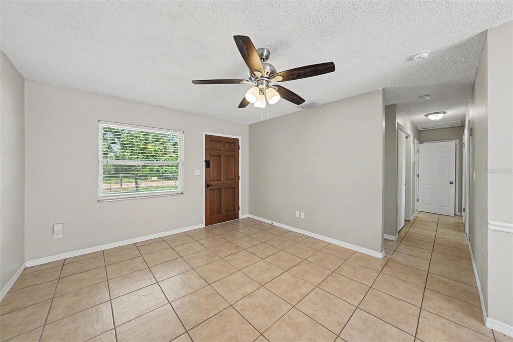 A room with light-colored walls, tile flooring, a ceiling fan, and a wooden front door — 10410 N 27TH STREET, TAMPA, FL