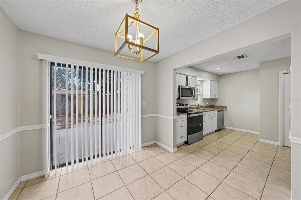 A dining area with tile flooring and a gold pendant light leads into a kitchen — 10410 N 27TH STREET, TAMPA, FL