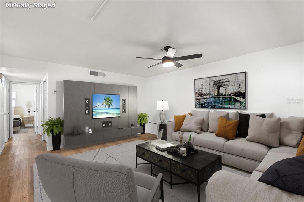 This virtually staged living room features a gray sectional sofa, a coffee table, and television — 2865 51ST STREET S UNIT 5, GULFPORT, FL