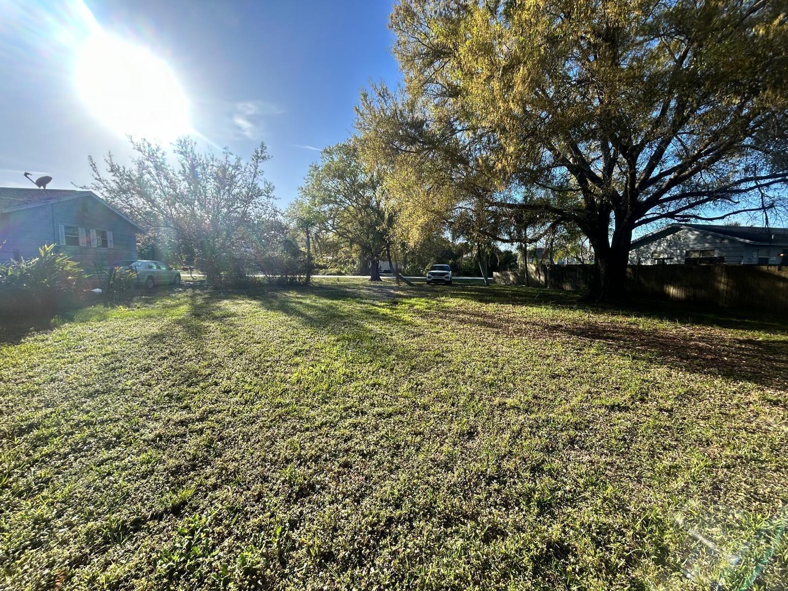 A large, grassy backyard features mature trees, a wooden fence, and two parked cars — 8922 102nd Avenue, Vero Beach FL 32967, VERO BEACH, FL