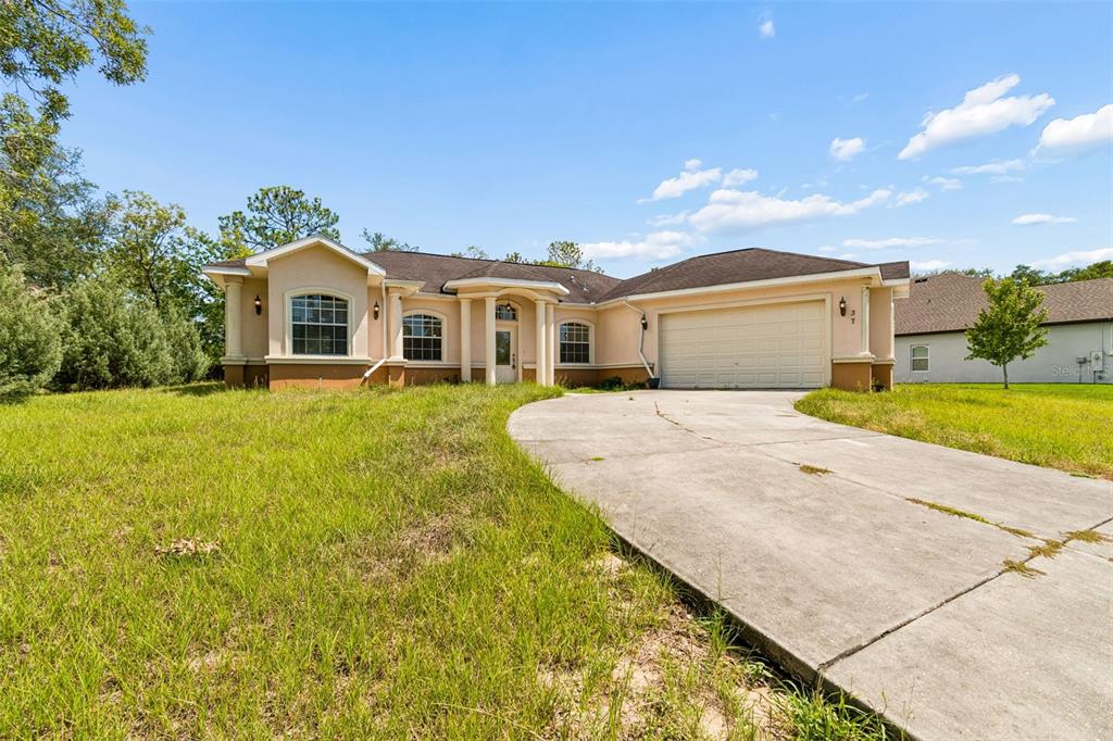 A single-story house with a beige stucco exterior, a two-car garage, and a concrete driveway — 37 GREENPARK BOULEVARD, HOMOSASSA, FL