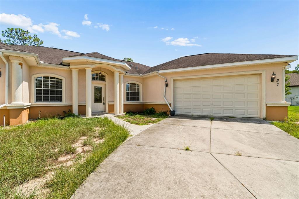 A single-story house with a beige stucco exterior, a two-car garage, and a columned entryway — 37 GREENPARK BOULEVARD, HOMOSASSA, FL