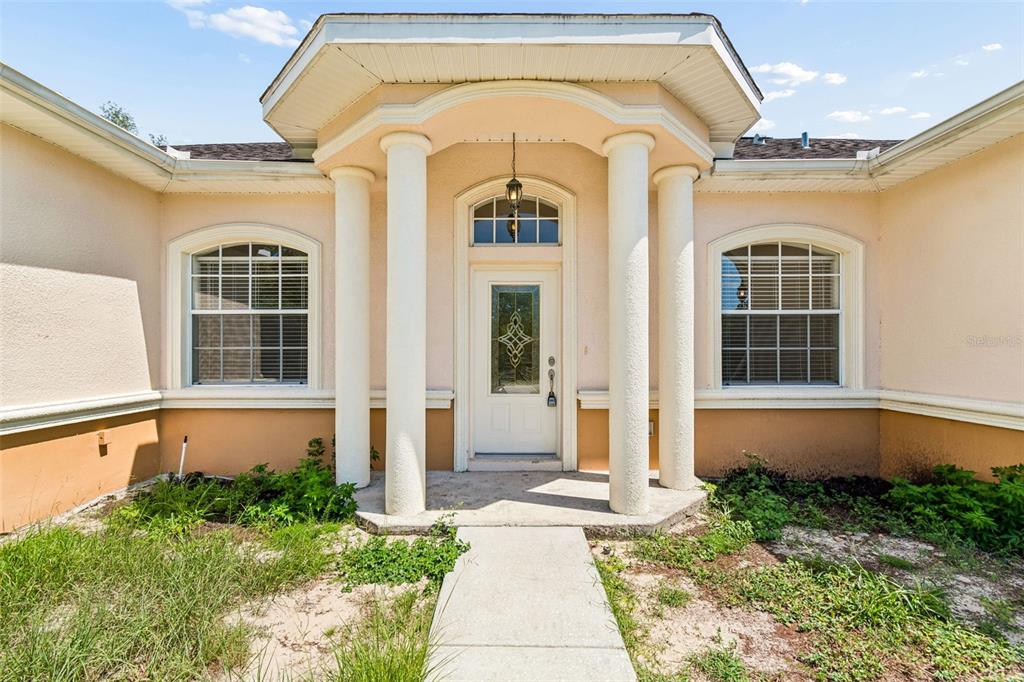 The exterior of a house features a columned entryway, a front door, and two windows — 37 GREENPARK BOULEVARD, HOMOSASSA, FL