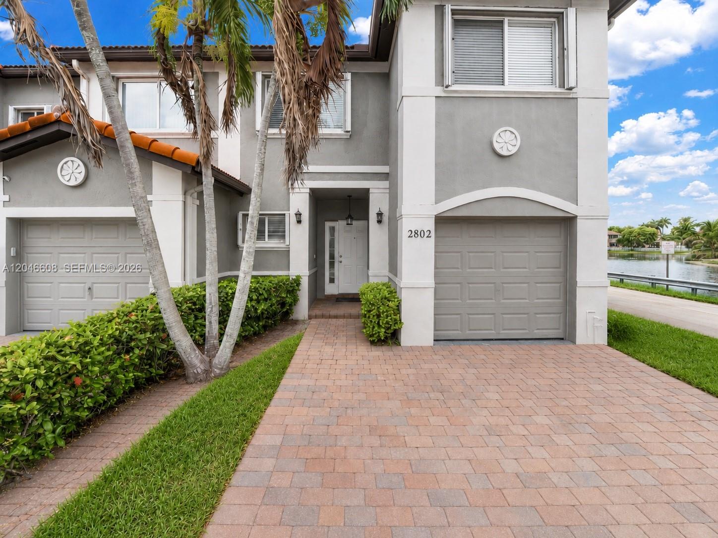 A two-story townhouse exterior features a gray facade, brick driveway, and an attached garage — 2802 SW 128th Way # B, Miramar FL 33027, MIRAMAR, FL