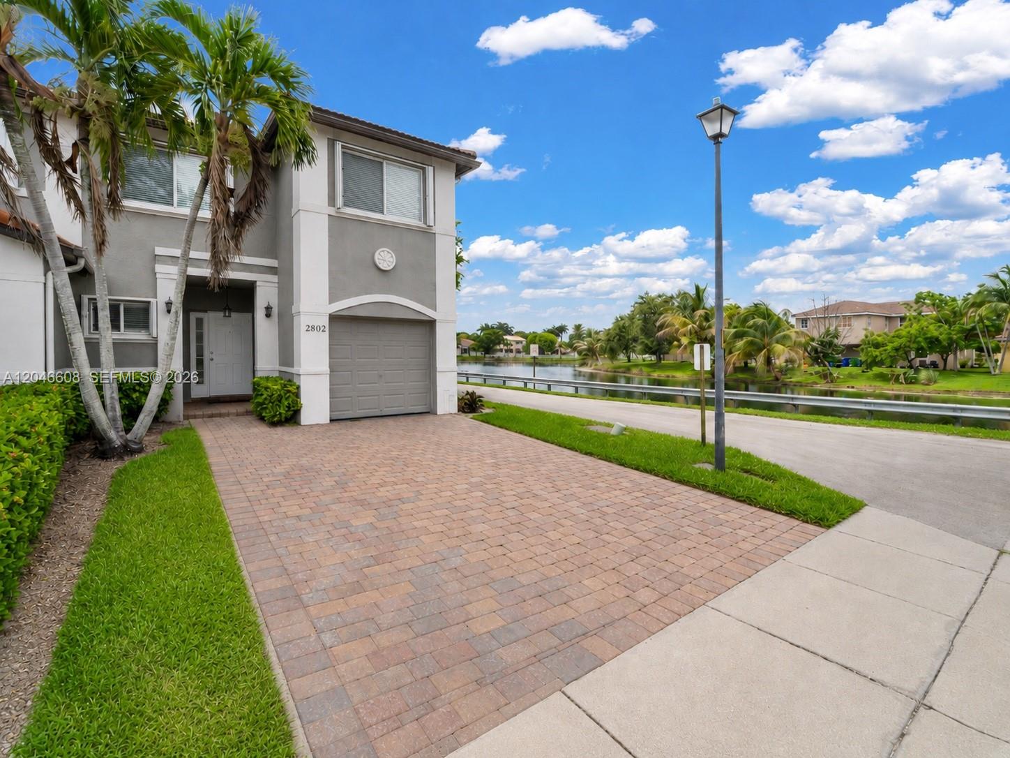 A two-story gray house with a paver driveway sits beside a lake and street — 2802 SW 128th Way # B, Miramar FL 33027, MIRAMAR, FL