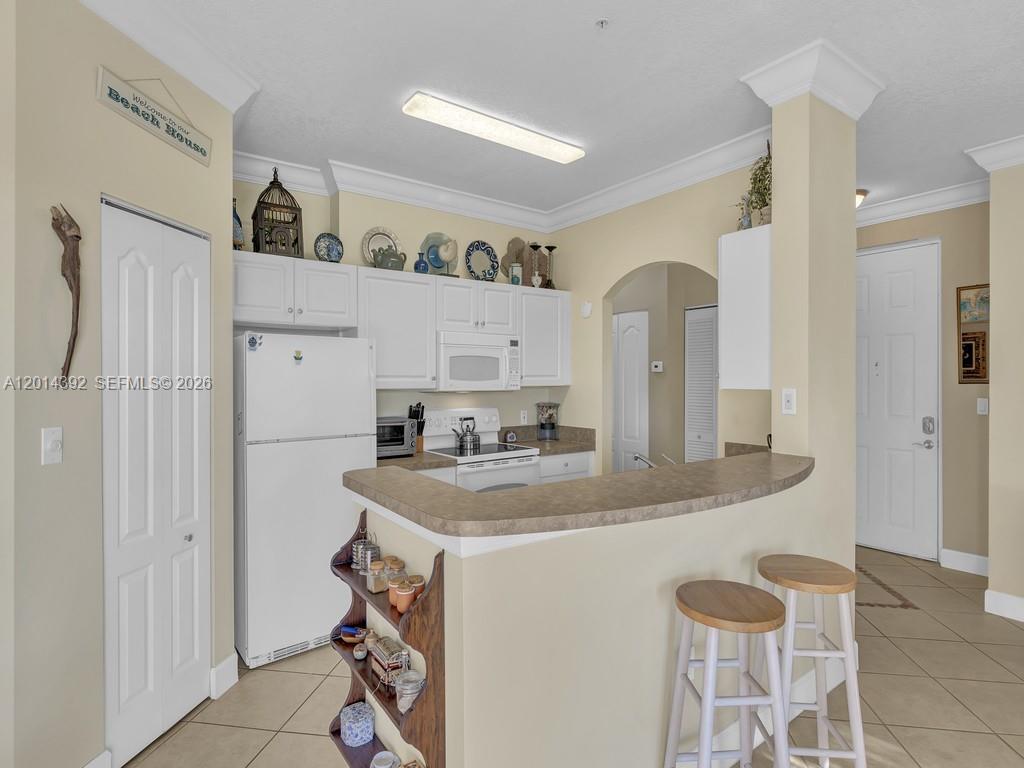 A kitchen features white cabinets, a breakfast bar with stools, and light-colored tile flooring — 5035 Fairways Cir # 305, Vero Beach FL 32967, VERO BEACH, FL