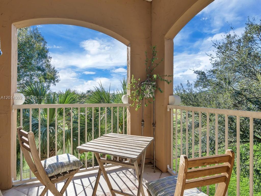 A balcony features a small wooden table and two chairs overlooking trees and sky — 5035 Fairways Cir # 305, Vero Beach FL 32967, VERO BEACH, FL
