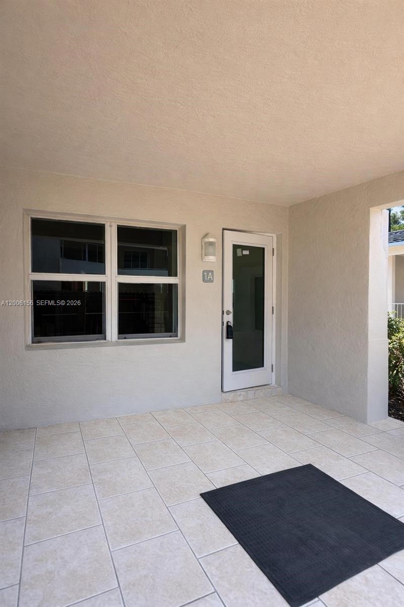A tiled patio leads to a white front door labeled 1A next to a window — MIAMI BEACH, FL