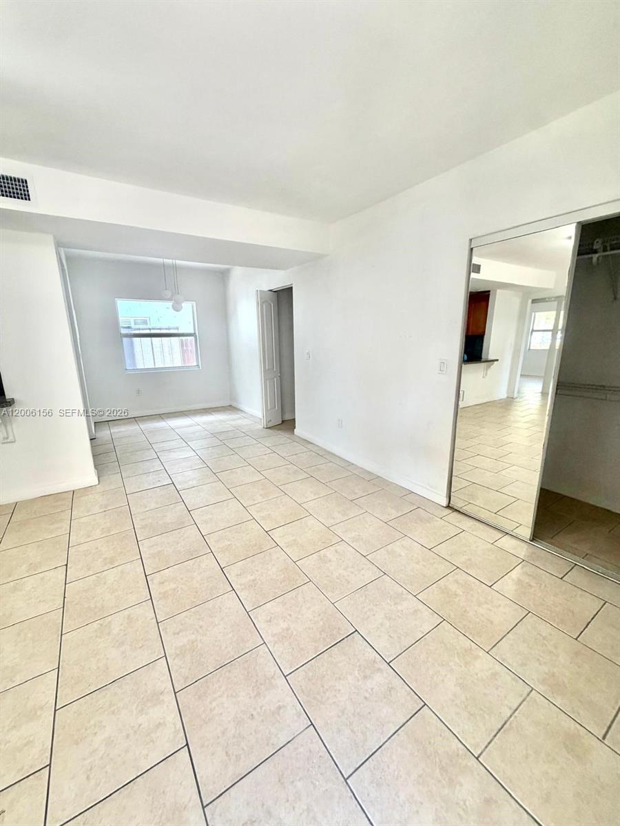 A room with light-colored tile flooring, white walls, and a mirrored closet door — MIAMI BEACH, FL