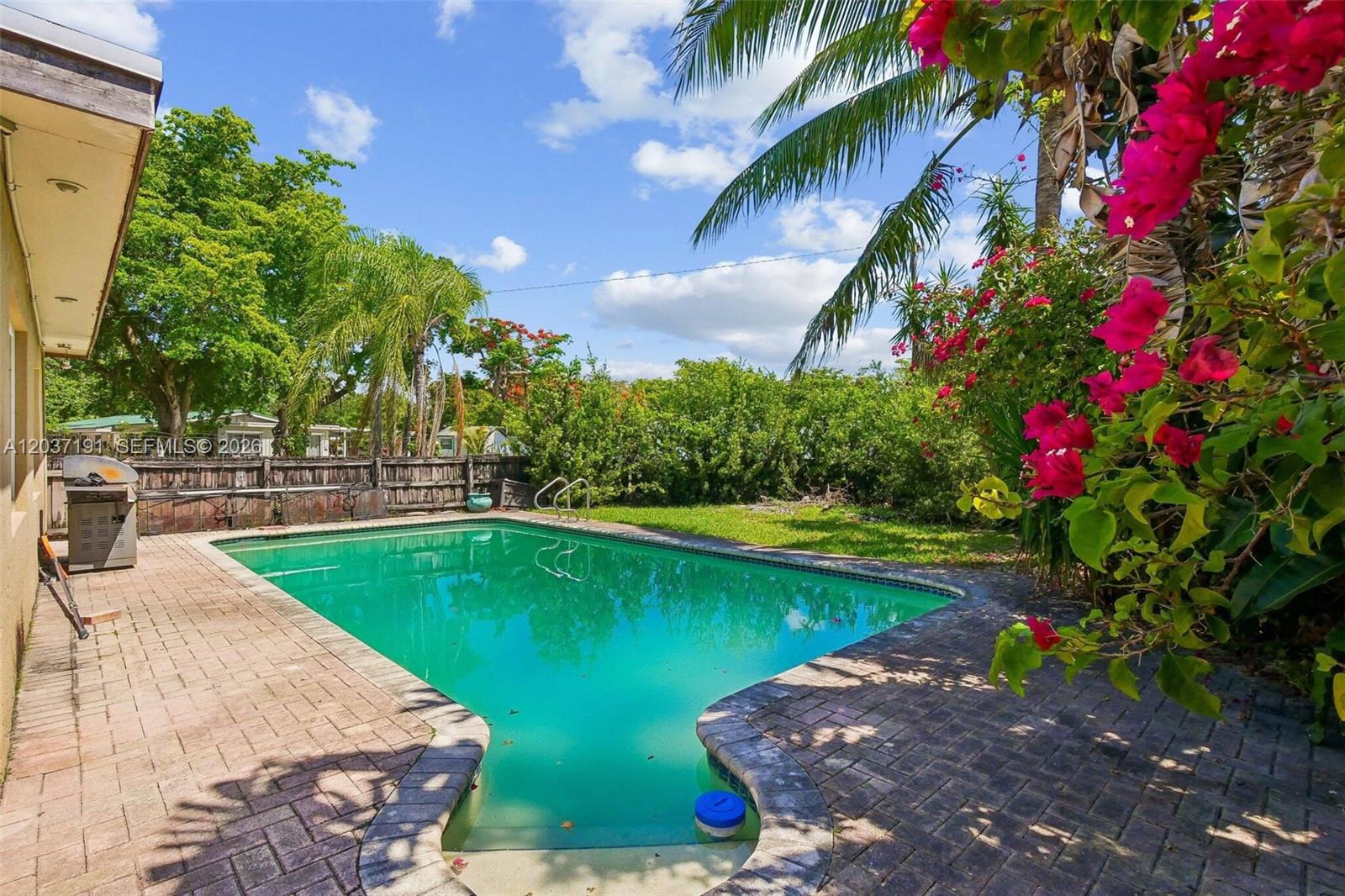 A backyard features a rectangular swimming pool surrounded by brick pavers and lush landscaping — 401 S 57th Ter, Hollywood FL 33023, HOLLYWOOD, FL