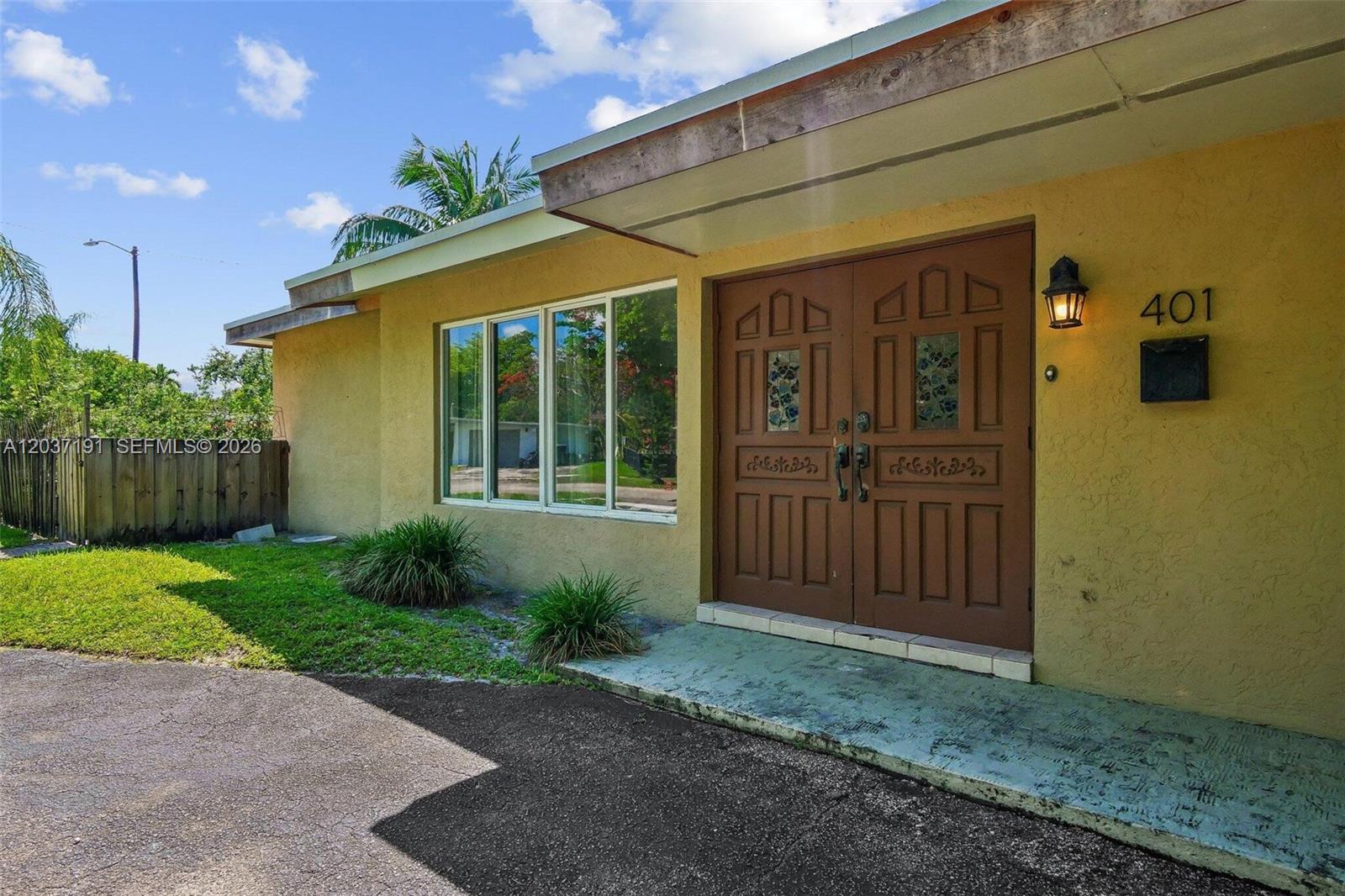 A yellow house exterior features a double brown front door and a large window — 401 S 57th Ter, Hollywood FL 33023, HOLLYWOOD, FL