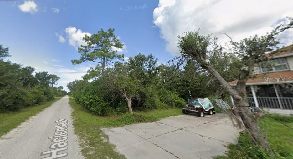 A gravel road runs alongside a concrete driveway and a wooded lot next to a house — 27198 & 27204 HACIENDA DRIVE, PUNTA GORDA, FL