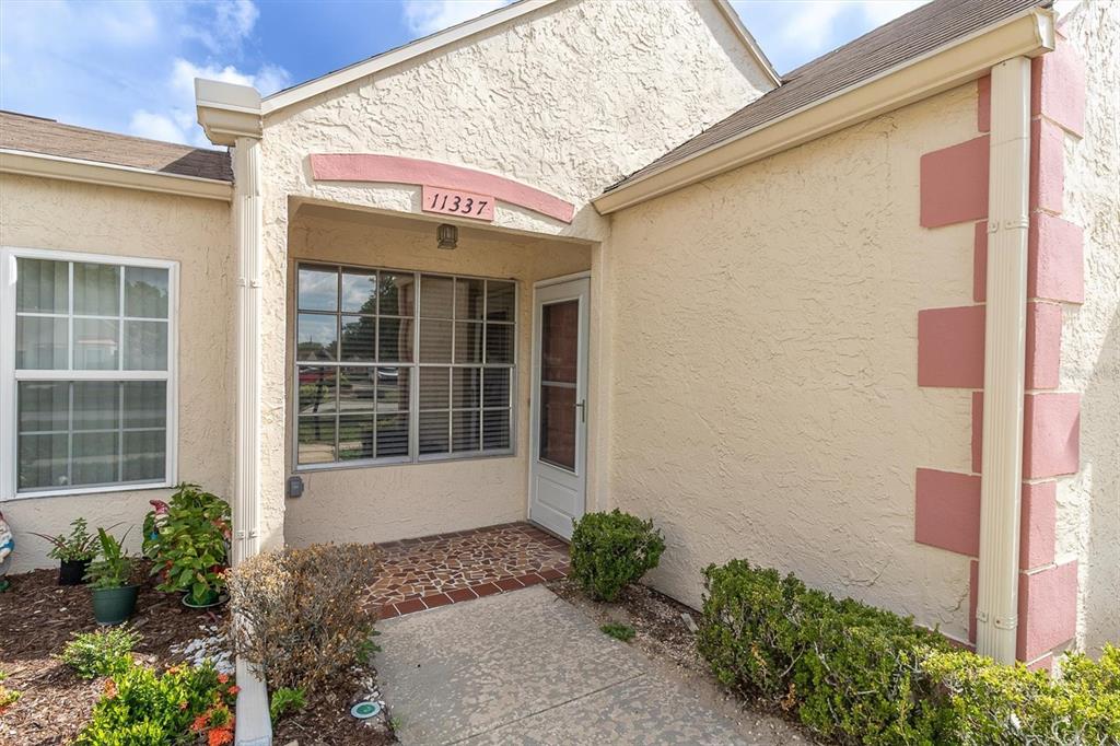 The exterior of a beige stucco home features a covered entryway with a tiled floor — 11337 VERSAILLES LANE, PORT RICHEY, FL