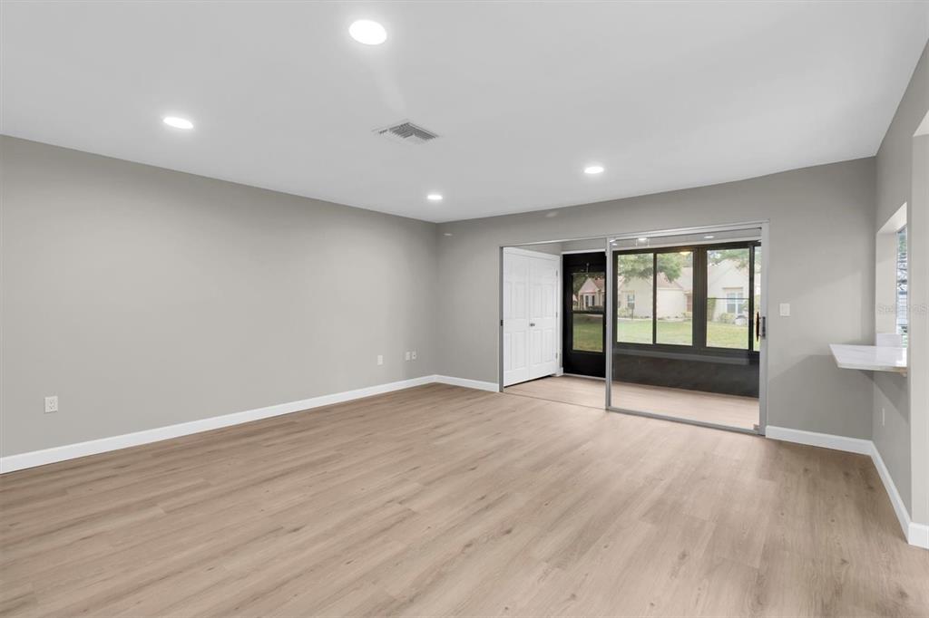 A spacious living room with light wood-look flooring, gray walls, and a sliding glass door — 11337 VERSAILLES LANE, PORT RICHEY, FL