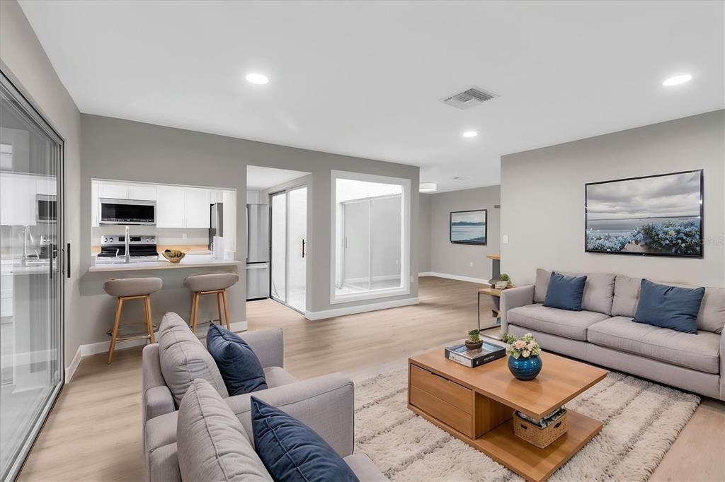 A living room with light wood floors, gray sofas, a coffee table, and an open kitchen — 11337 VERSAILLES LANE, PORT RICHEY, FL