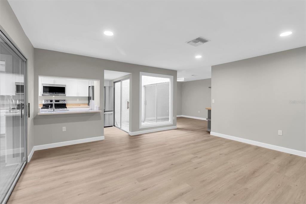 A living area with light wood-look flooring, gray walls, and a kitchen pass-through window — 11337 VERSAILLES LANE, PORT RICHEY, FL