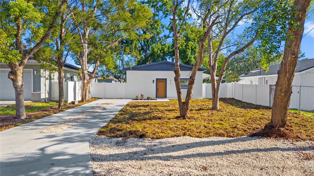 A white single-story house features a wooden front door, a concrete driveway, and mature trees — 815 W MINNEHAHA STREET, TAMPA, FL