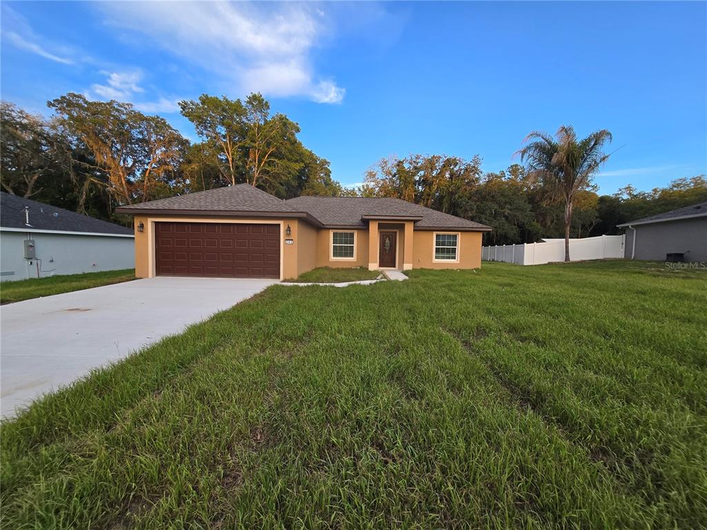A single-story house with a brown garage door, tan stucco exterior, and a grassy yard — 203 EMERALD ROAD, OCALA, FL