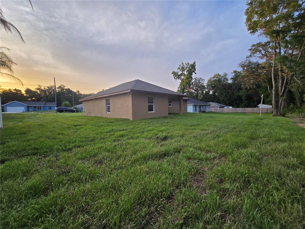 A view of the side and rear exterior of a tan house with a yard — 203 EMERALD ROAD, OCALA, FL