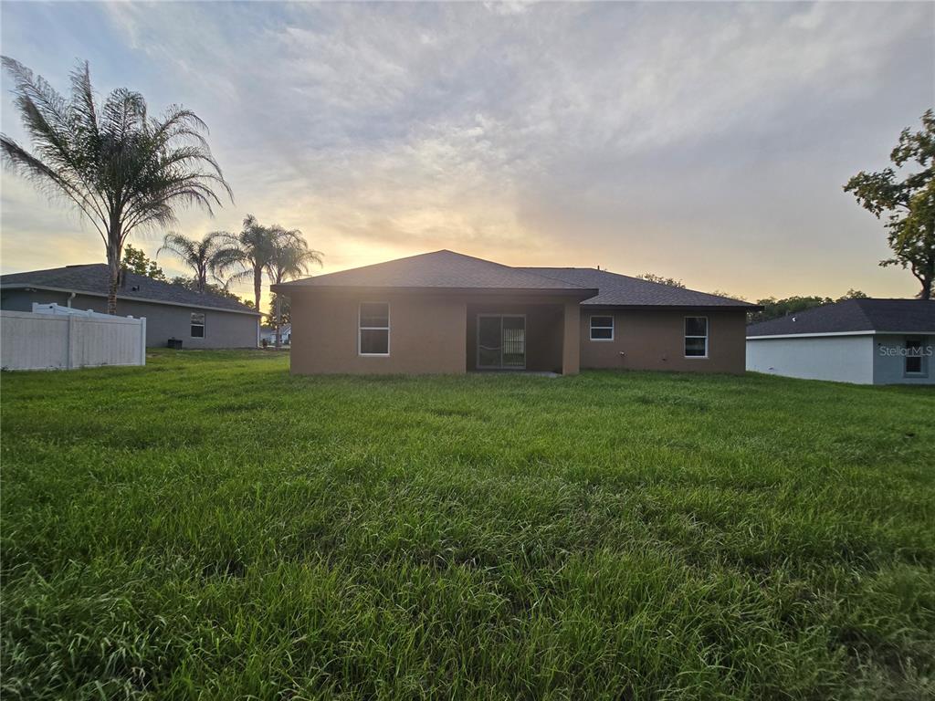 The rear exterior of a single-story house features a covered patio and a grassy yard — 203 EMERALD ROAD, OCALA, FL