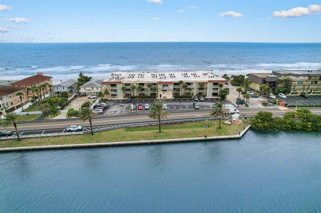 An aerial view shows a multi-story apartment building situated between a road and the ocean — 50 GULF BOULEVARD UNIT 206, INDIAN ROCKS BEACH, FL