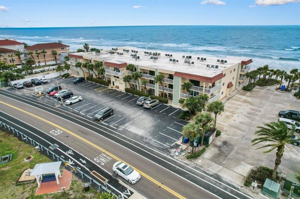 An aerial view shows a multi-story beachfront apartment building with a parking lot and ocean — 50 GULF BOULEVARD UNIT 206, INDIAN ROCKS BEACH, FL
