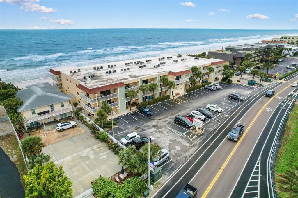 An aerial view shows a multi-story beachfront apartment building with a parking lot and road — 50 GULF BOULEVARD UNIT 206, INDIAN ROCKS BEACH, FL