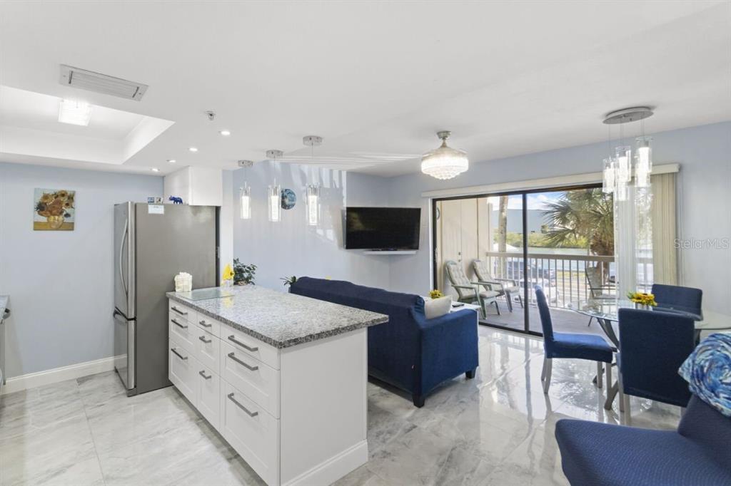 An open-concept kitchen and living area features white cabinetry, granite countertops, and a balcony view — 50 GULF BOULEVARD UNIT 206, INDIAN ROCKS BEACH, FL