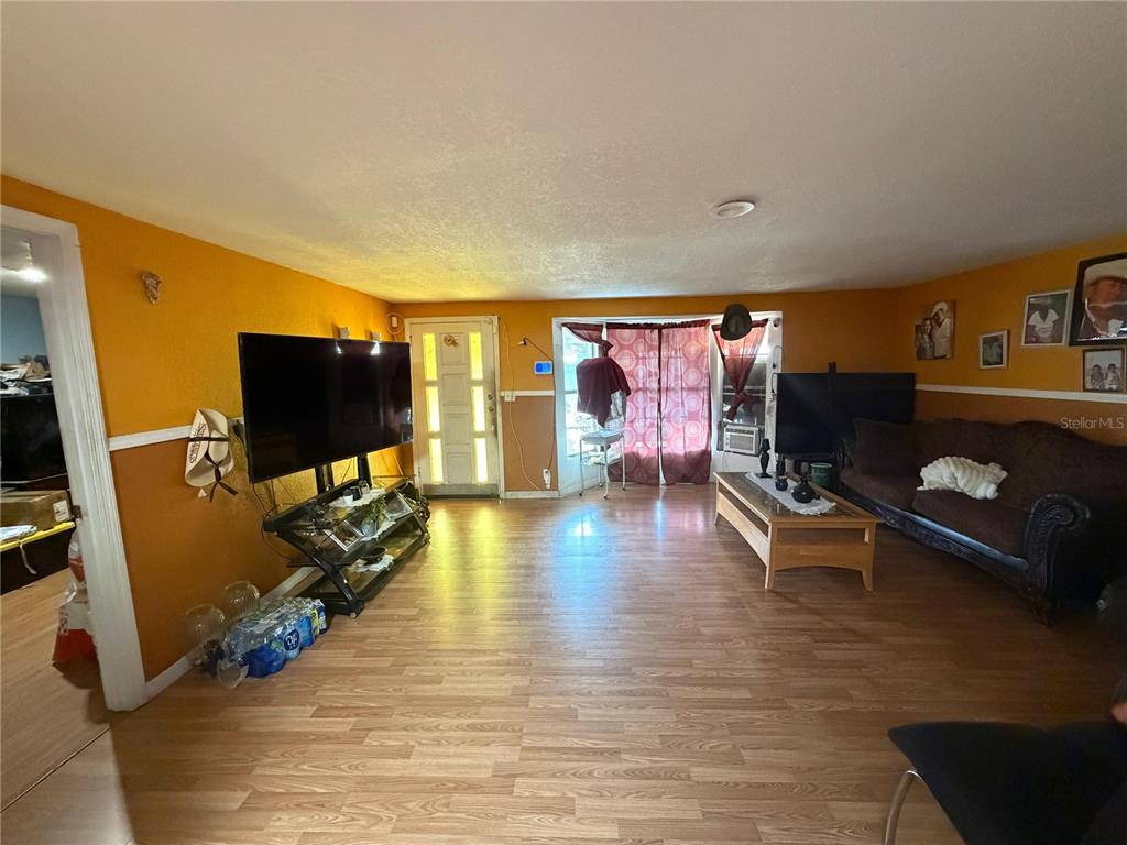 A living room features orange walls, wood-look flooring, a television, and a brown sofa — 2300 SMITH ROAD, HAINES CITY, FL