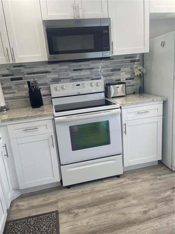 A kitchen features white cabinets, a white electric range, a microwave, and a tiled backsplash — 5724 LA PUERTA DEL SOL BOULEVARD UNIT 248, ST PETERSBURG, FL