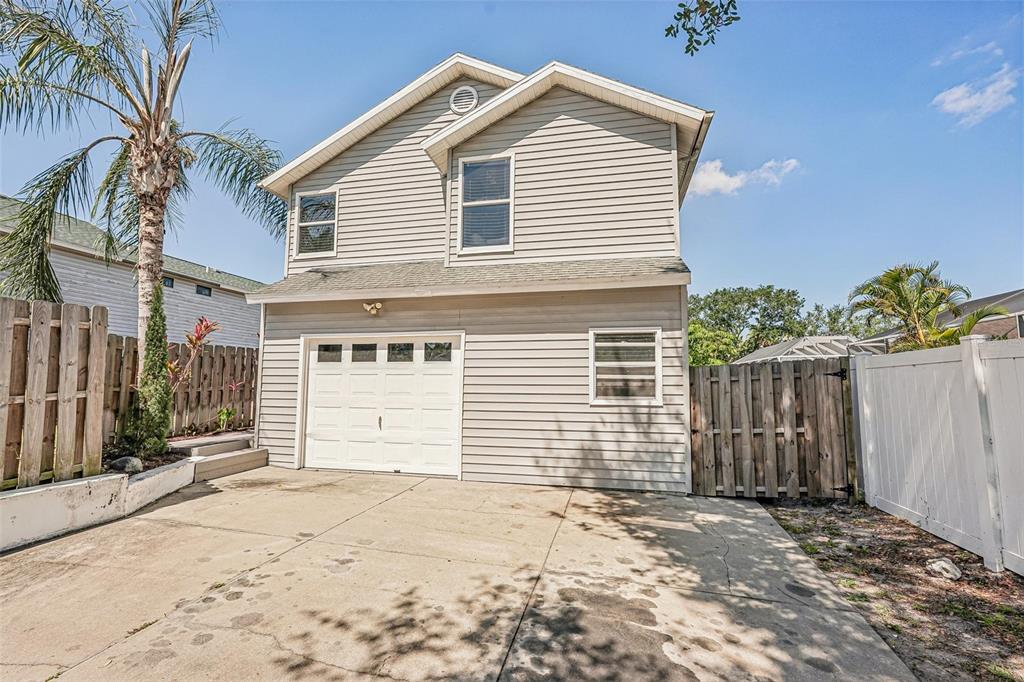 A concrete driveway leads to a two-story house with a white garage door and fences — 5102 MOELLER AVENUE, SARASOTA, FL