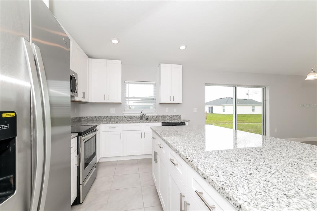 A kitchen features white cabinets, granite countertops, stainless steel appliances, and a large center island — 280 BECKENHAM DRIVE, KISSIMMEE, FL