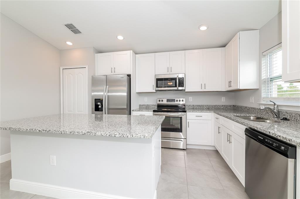 A kitchen features white cabinets, granite countertops, stainless steel appliances, and a breakfast bar — 280 BECKENHAM DRIVE, KISSIMMEE, FL